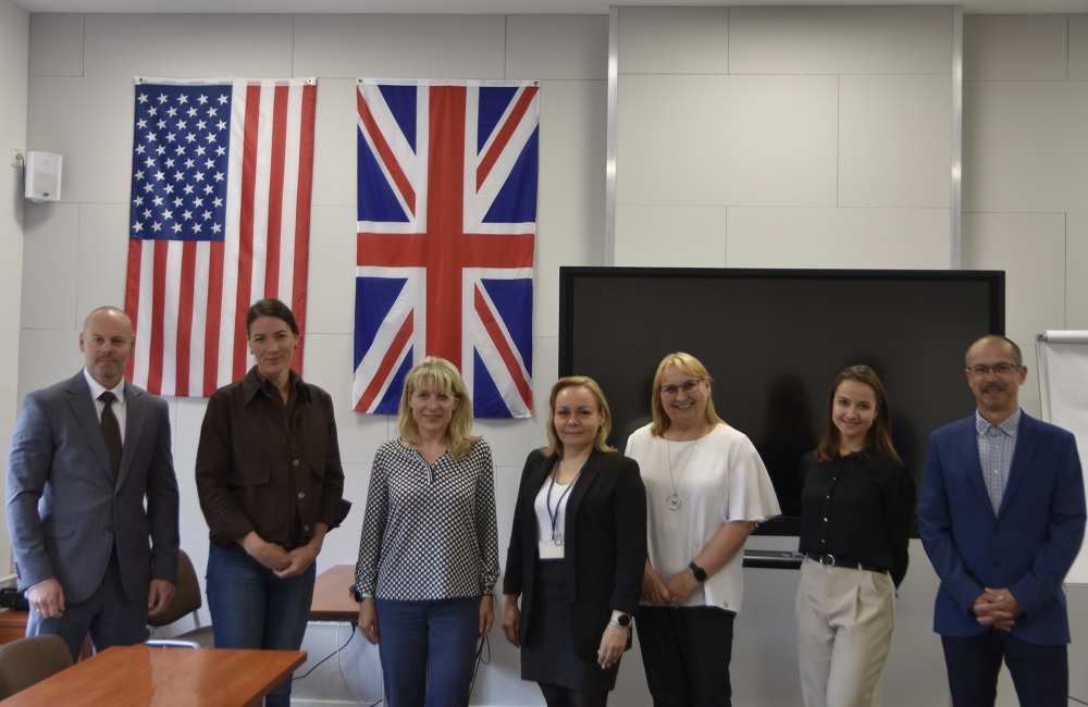 Uczestnicy seminarium językowego w Koszalinie stoją na tle flag Stanów Zjednoczonych i Wielkiej Brytanii.