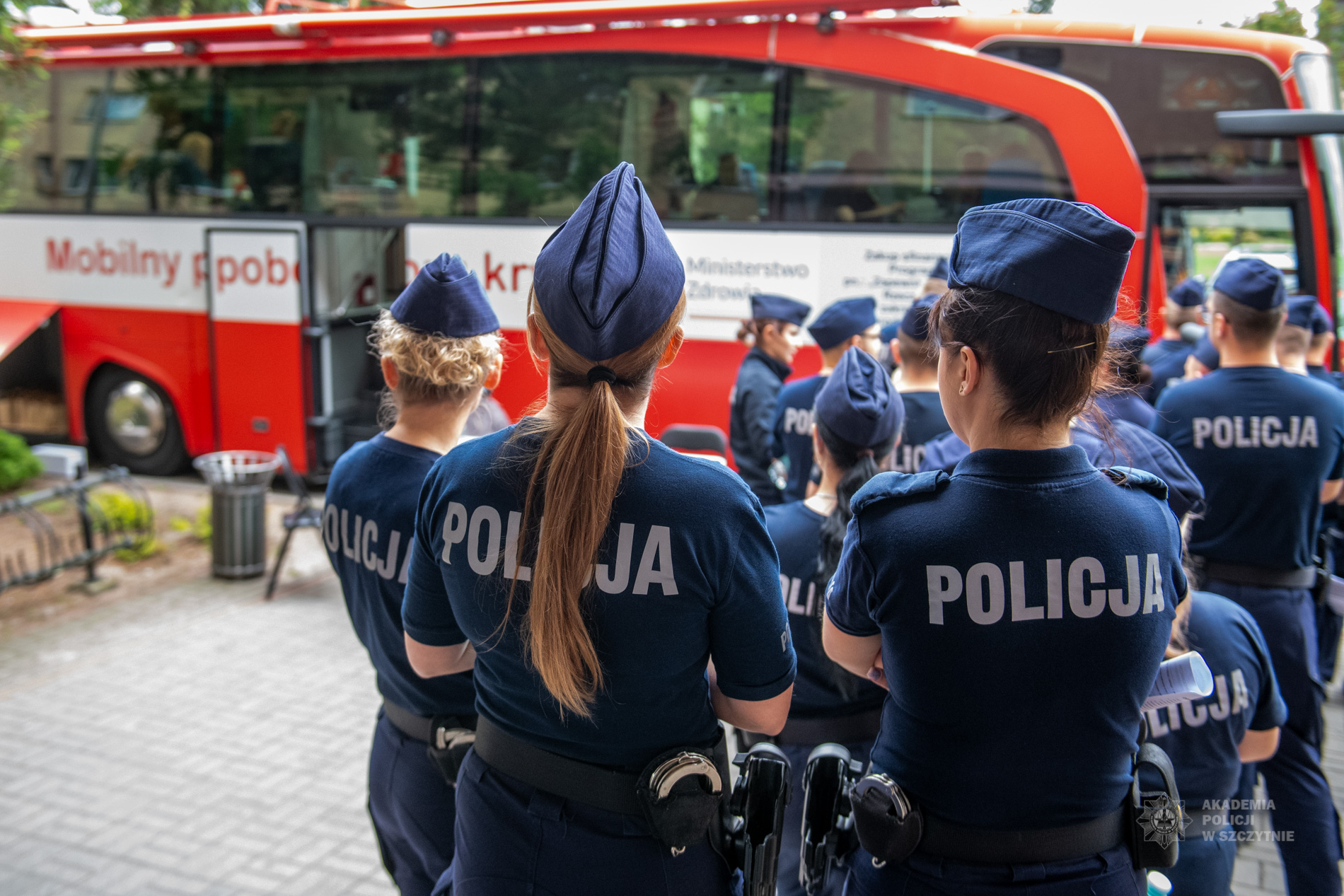 Policjantki i policjanci stoją przed mobilnym punktem poboru krwi.