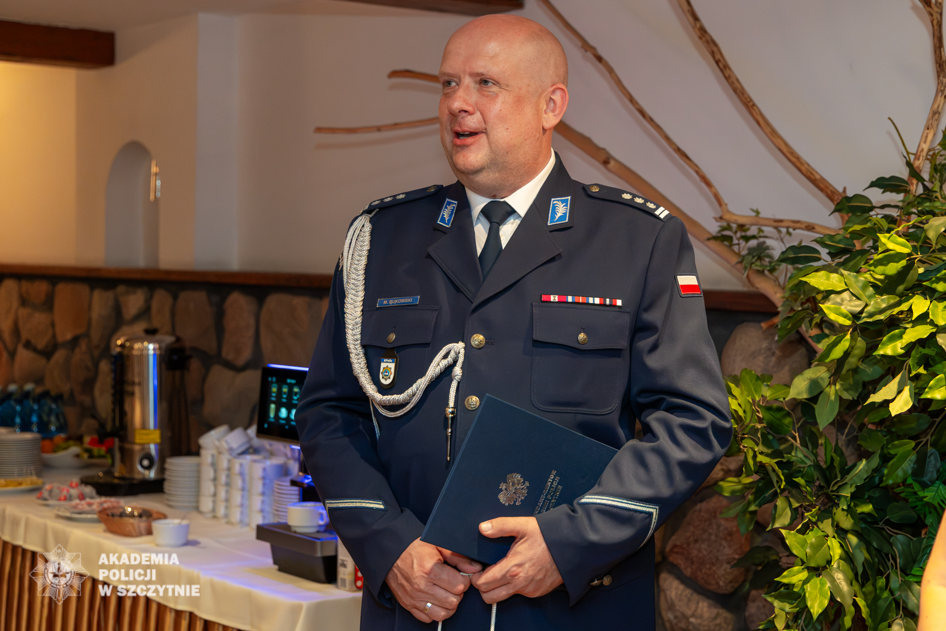 Inspektor Michał Bukowski stoi w policyjnym mundurze wyjściowym ze sznurem oficerskim podczas pożegnania.